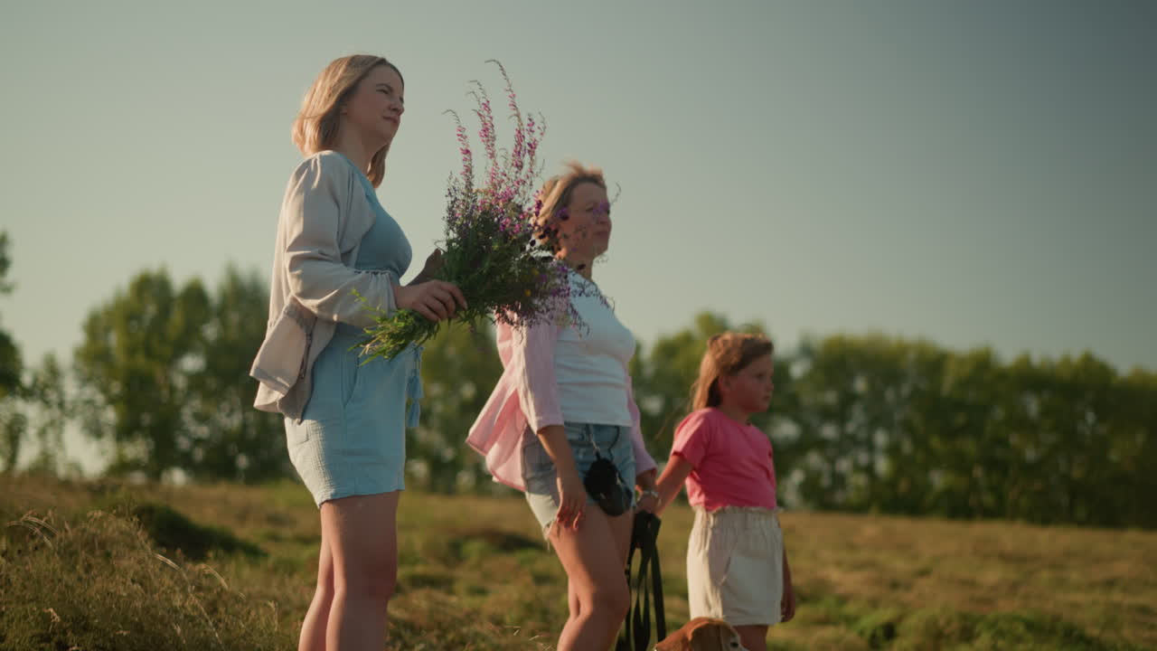 젊은 여성은 가게 미소 짓고, 보라색 꽃의 꽃줄기를 들고 멀리 을 가리키며, 밝은 빛의 날, 빛이 그녀의 얼굴에서 반사되는 바에 서서 평화로운 순간을 즐기고 있습니다.