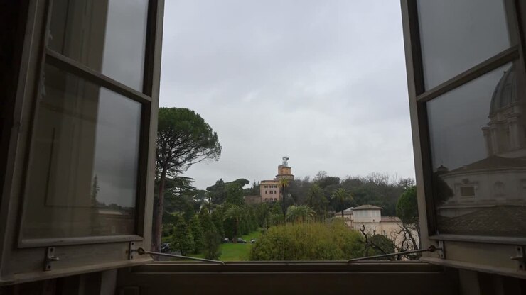 A panoramic window perspective looking over the meticulously manicured lawns fountains and Renaissance architecture of the Vatican Gardens from the museum galleries