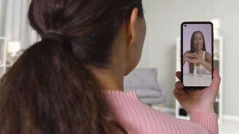 Primer-Plano-De-Una-Mujer-En-Casa-Mirando-Un-Vídeo-De-Demostración-De-Productos-De-Belleza-En-Un-Teléfono-Móvil