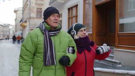 Senior-old-couple-grandmother-and-grandfather-in-colorful-winter-jackets-walking-in-winter-city