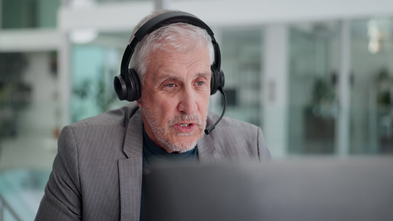 Fokuseret ældre mand med headset arbejder ved computer på kontor.