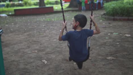 Kid-in-a-blue-shirt-in-a-swing-by-himself-in-the-playground-in-slowmotion