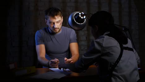 man forced to write a confession woman detective adamant man unshaven and in handcuffs forced to write a confession woman detective adamant they sit at the table where stacked folders with documents and evidence glow lamp emotions subordination of