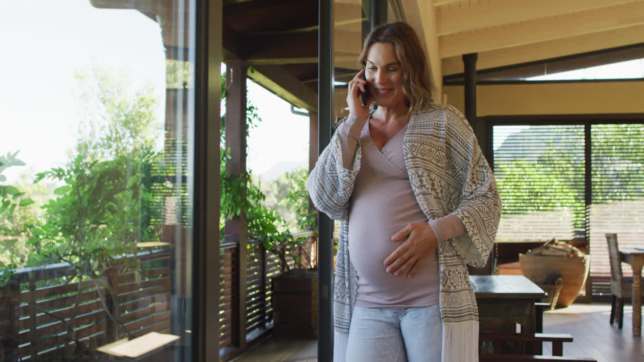 Happy caucasian pregnant woman standing on patio and having phone call