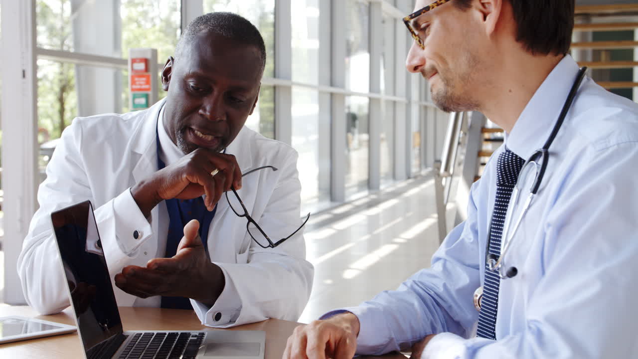 dos médicos varones que se reúnen sentados alrededor de la mesa en el hospital