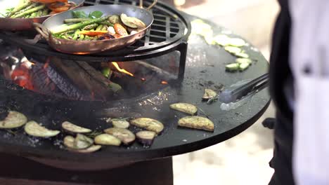 the cook roasts the courgettes. grilled vegetables. round bowl-shaped grill with a fire inside.