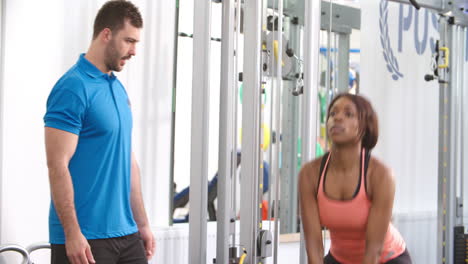 mujer usando un peso de kettlebell con un entrenador en un gimnasio