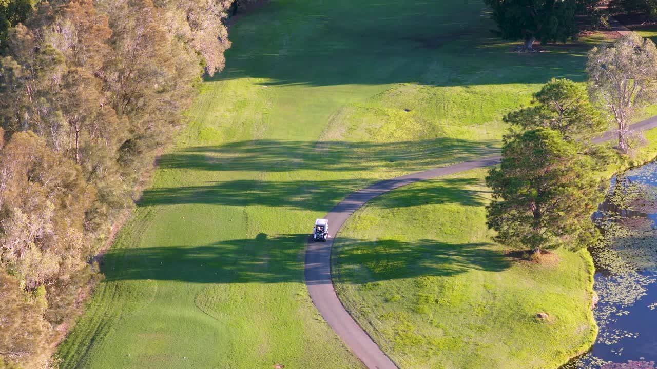 Drone footage captures a serene golf course landscape with a winding cart path, surrounded by lush greenery and trees