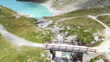 close flight over small mountain bridge revealing turquoise blue mountain lake in mountain scenery in switzerland alps