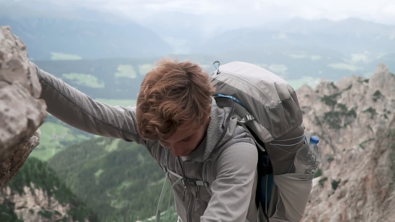 Slow motion shot of exhausted young man climbing up steep rocks with beautiful landscape in the backdrop. Dolomites, Italy