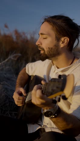 man playing guitar outdoors at sunset