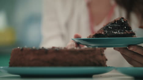 Close-up-of-female-hand-put-sweet-cake-on-plate.-Brown-cake-dessert