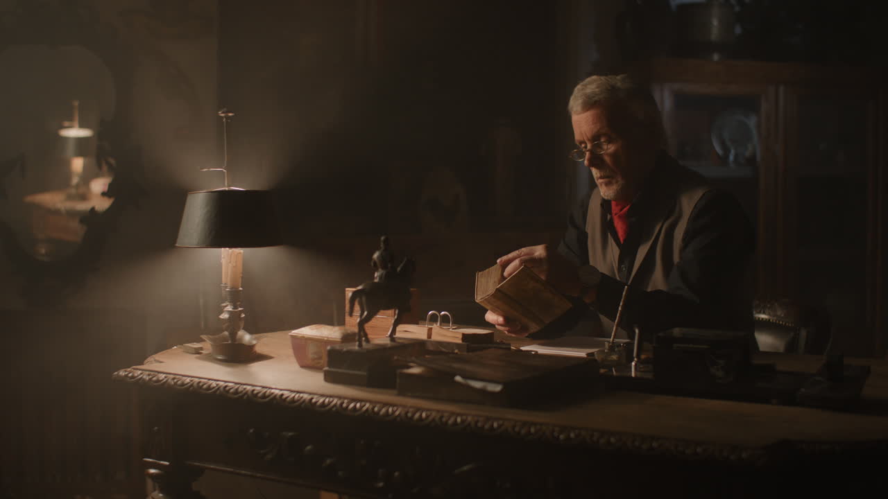 Old passionate man sits down to his desk, put on the glasses and writes a letter