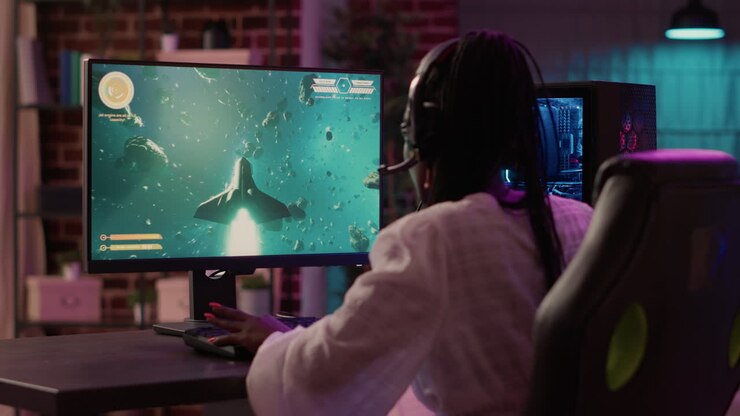 Ragazza afroamericana appassionata di videogiochi che gioca a un simulatore di sparatutto spaziale con una configurazione da gaming su PC, vista da sopra la spalla