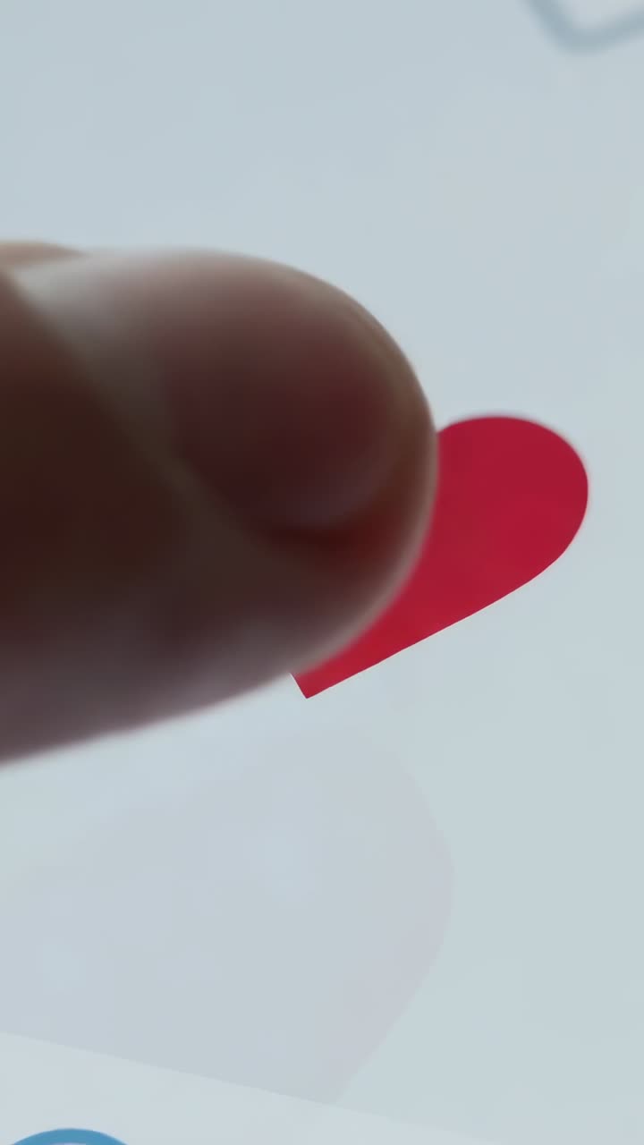 Video verticale: un dito tocca un cuore grigio su uno schermo portatile, riempiendo il cuore di rosso, punto blu