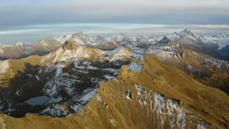 Slow-high-altitude-orbit-revealing-distant-Alpine-snowy-summits-at-sunset-Autumn-colors,-Valais---Switzerland
