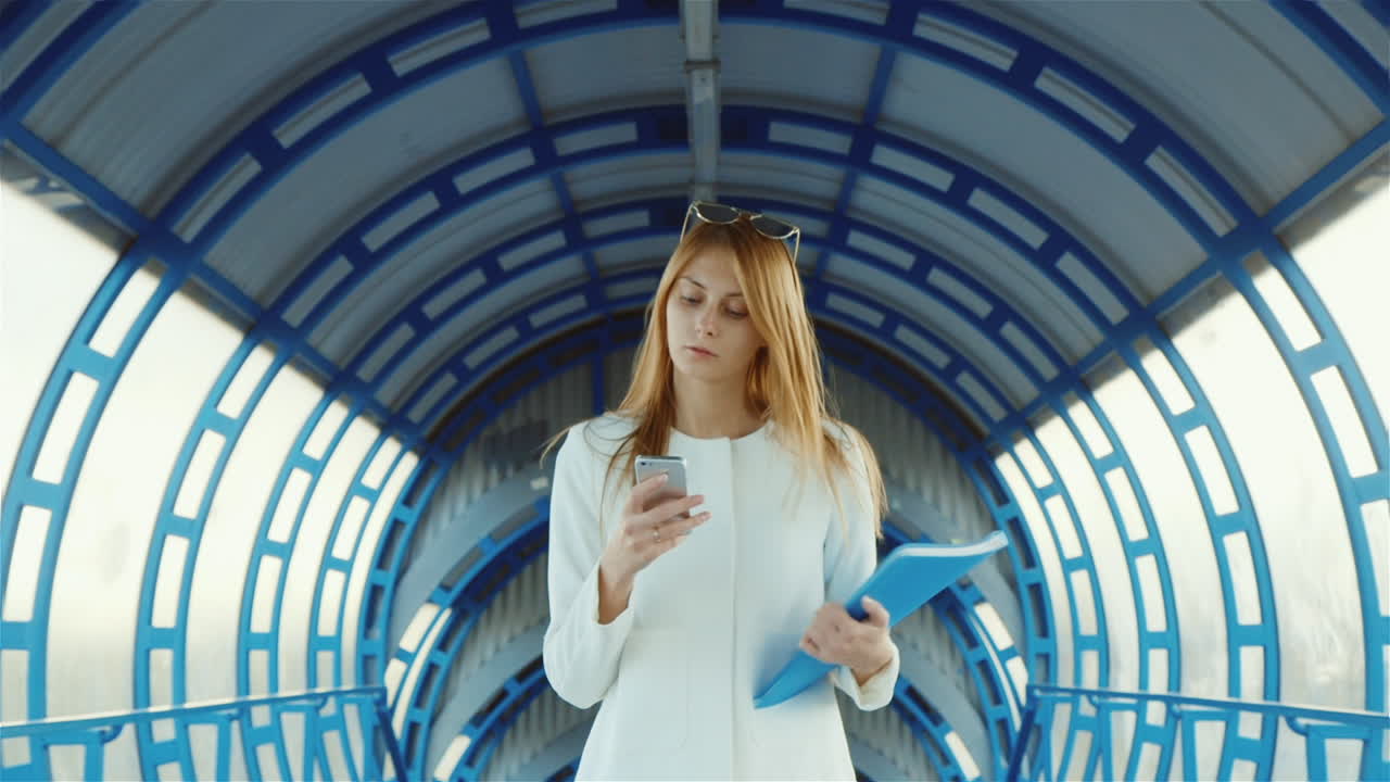 Donna d'affari in tailleur che parla in un moderno passaggio, tiene una cartella con documenti e il telefono.
