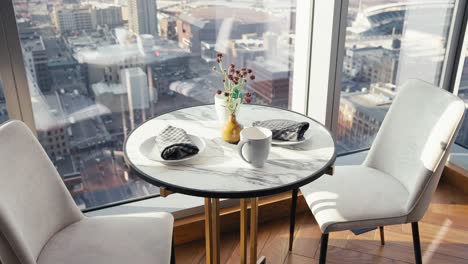 a small table set in the kitchen of a luxury high rise condo next to large glass windows showing the city beneath it