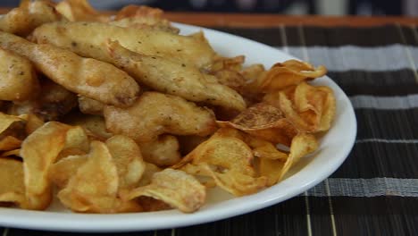 Plato-De-Pescado-Y-Patatas-Fritas-Servido-En-Un-Gran-Plato-Blanco-Encima-De-Una-Tabla-De-Corte-De-Madera-Con-Movimiento-Deslizante-Moviéndose-Hacia-Los-Lados