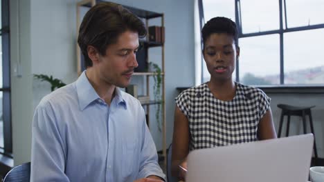 diverse business colleagues sitting at desk using laptop going through paperwork in office