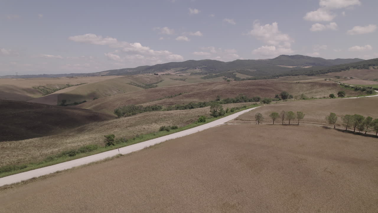 tomada de avión no tripulado de carreteras sinuosas y campos agrícolas dorados en la toscana, italia paisaje en un día soleado con cielo azul y nubes en el horizonte