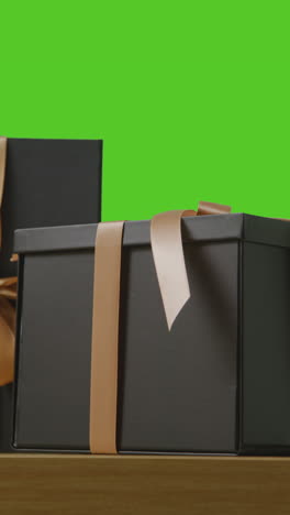 video vertical de regalos en cajas envueltas en regalos decoradas con cinta en la mesa disparado contra una pantalla verde 1
