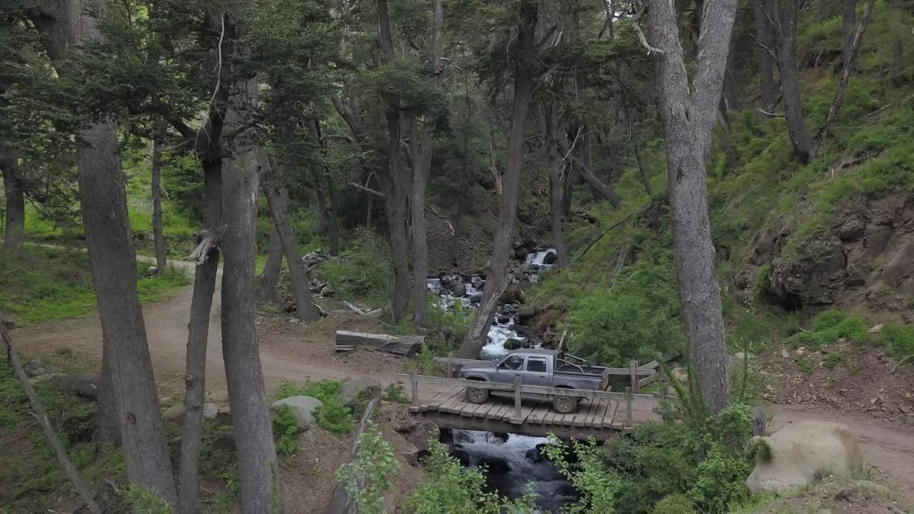 숲 한가운데 있는 개울 위의 작은 나무 다리를 지나가는 픽업 차량의 인상적인 전망