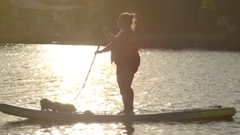 woman paddle boarding in sparkling lake sunset slomo