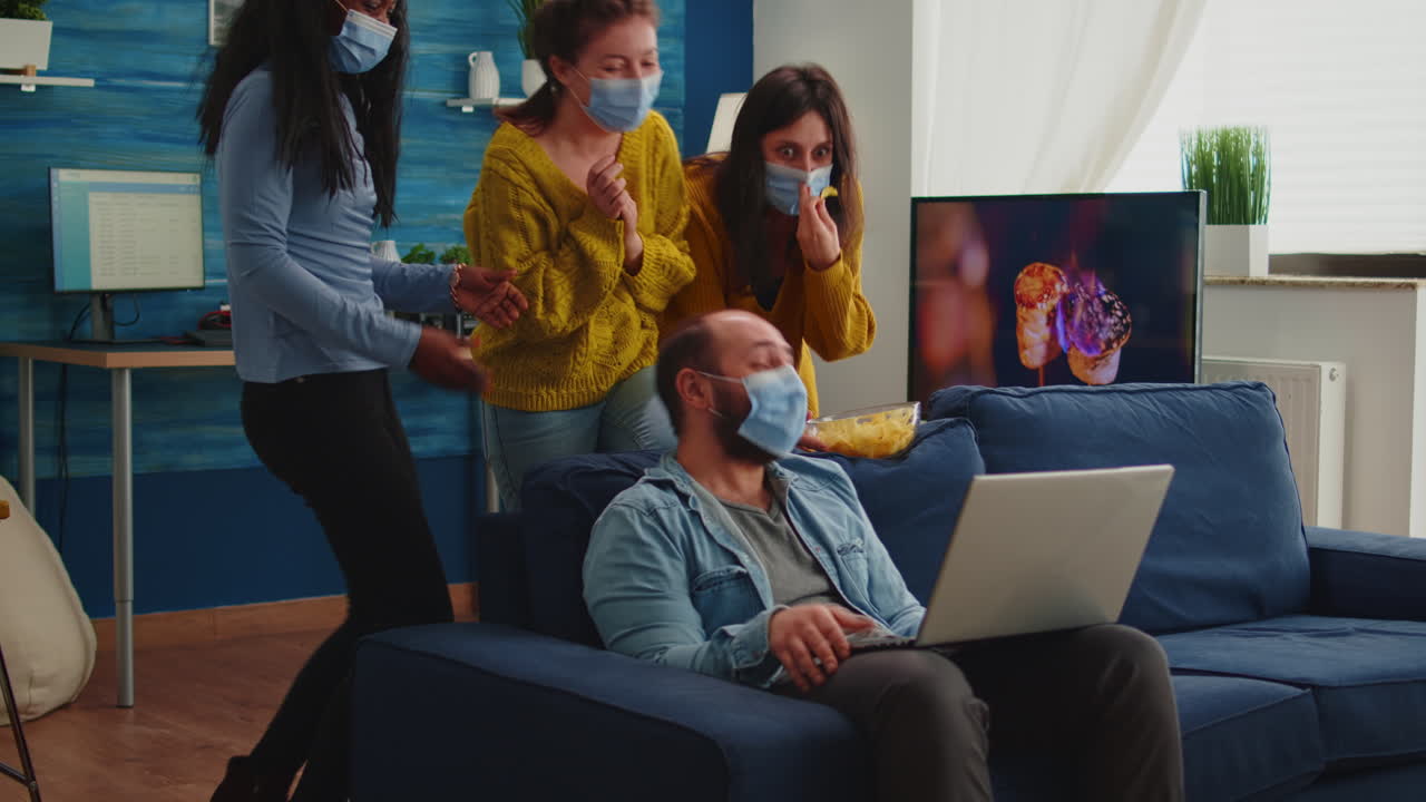 Multi ethnic friends wearing face mask eating snacks using laptop