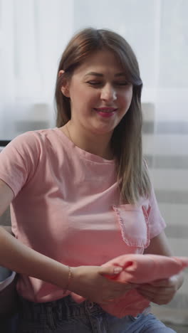 smiling mother folds garment looking at daughter helping with belongings in living room. happy family do chores together at home. clean laundry