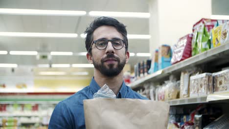 hombre serio con bolsa de papel en un supermercado