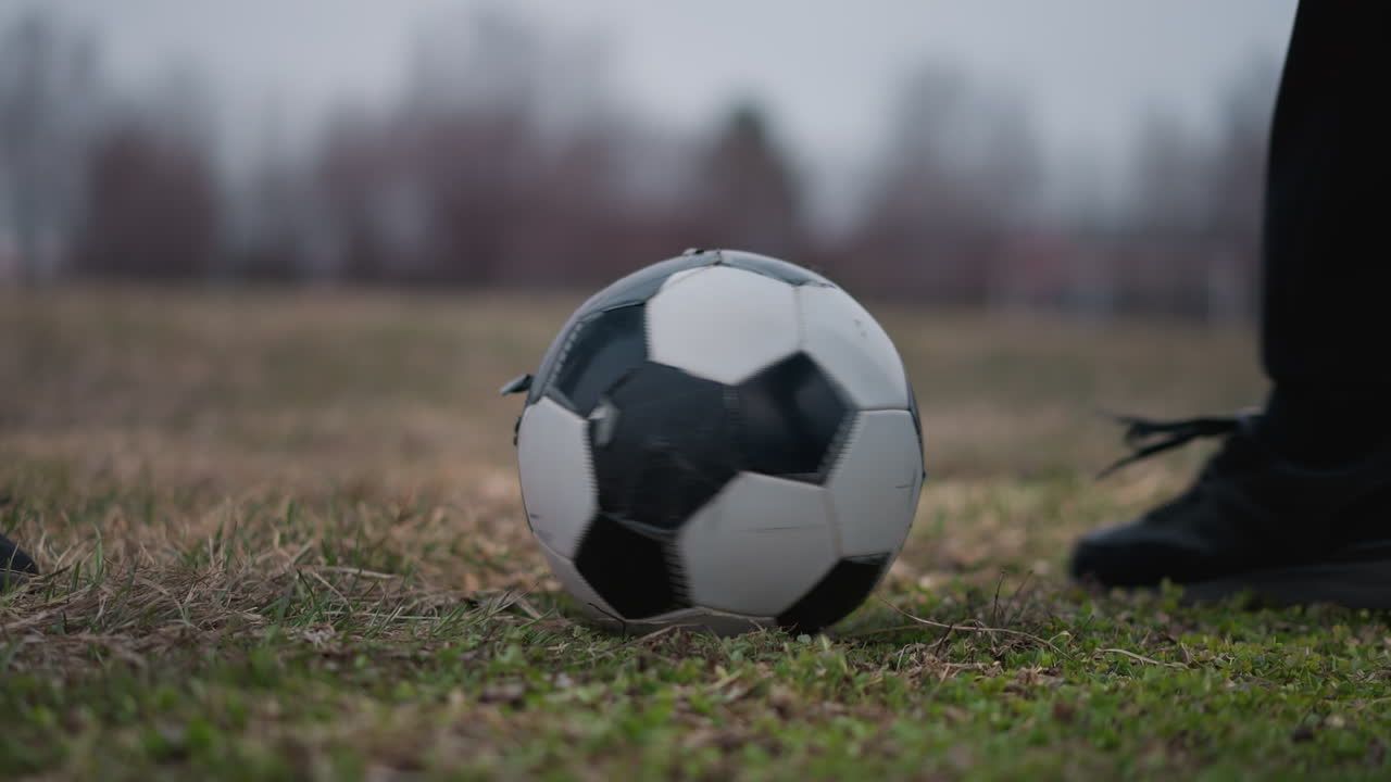 Close-up of someone stopping a rotating soccer ball with their left foot on a grassy field, with a blur background