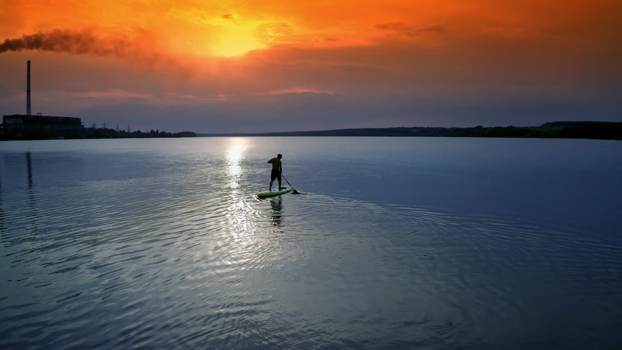 Man sailing on river. Sports training on water against beautiful sunset. Athlete is rowing on the evening water while standing with an oar. Water sports.