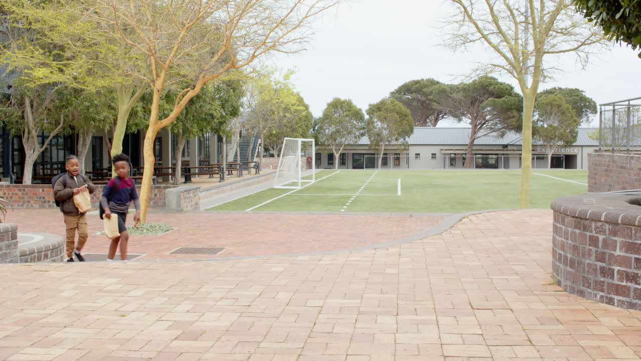 Walking with backpacks and lunch bags, multiracial boys chatting happily at school