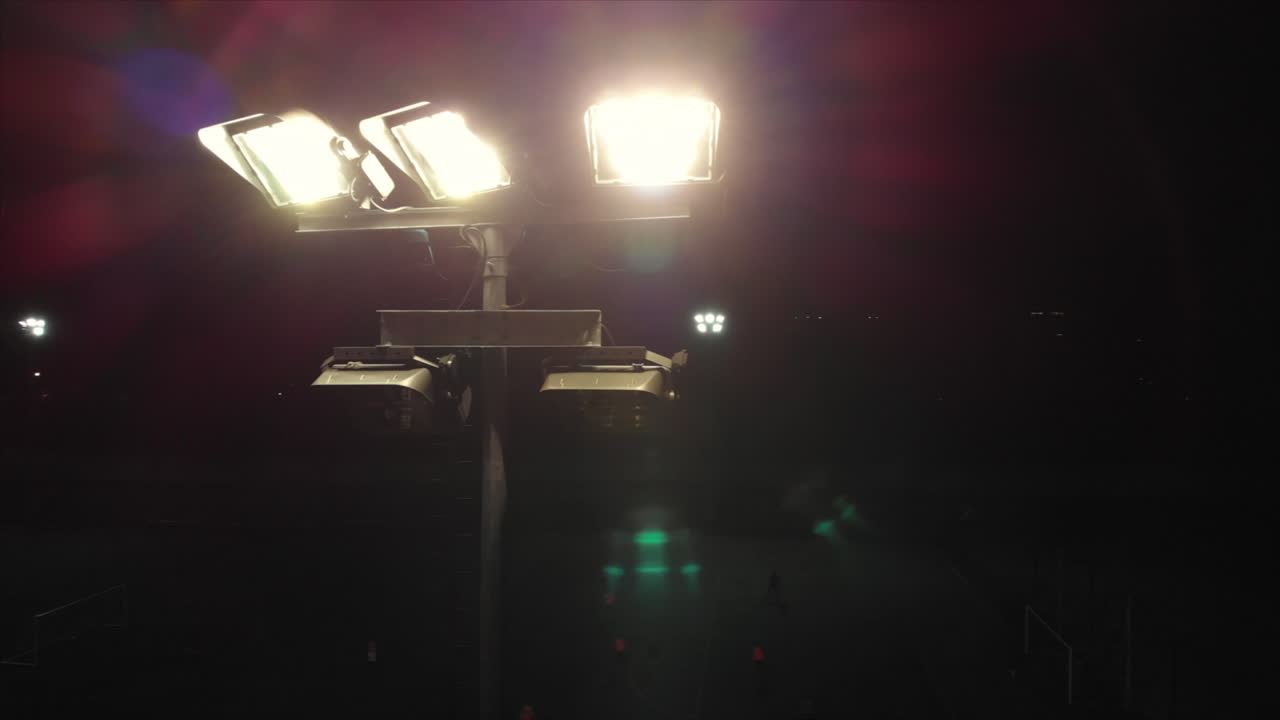 toma aérea alrededor de un reflector en un campo de fútbol, gente jugando al fútbol en el fondo, bengalas coloridas