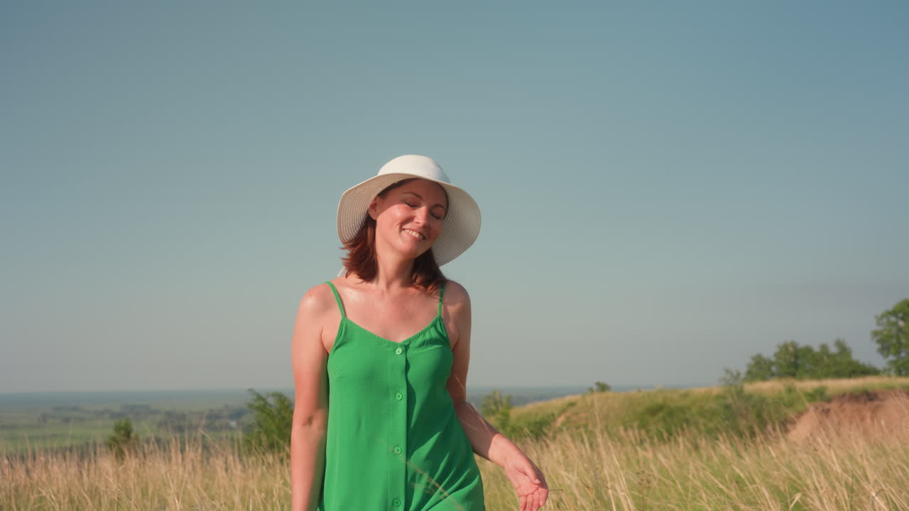 joyful woman in green dress lifts arms with eyes closed, embracing fresh air and sunlight in wide open natural field under clear blue sky, radiating peace, happiness, and connection with nature