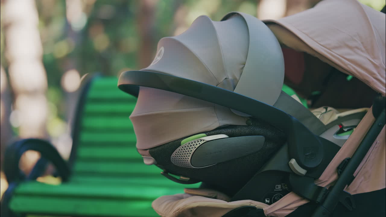 Young mother sitting on a park bench next to a stroller, enjoying a peaceful outdoor moment with her baby