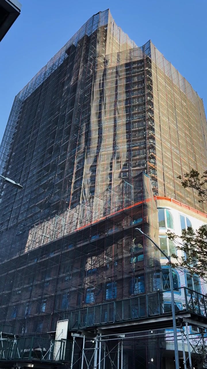 Edificio de gran altura en construcción con malla de andamios en un día soleado y despejado
