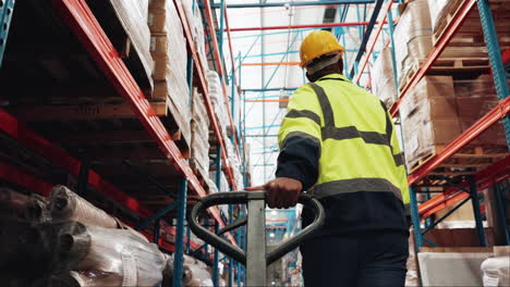 a warehouse worker in a yellow vest and hard hat pushes a hand truck down a narrow aisle