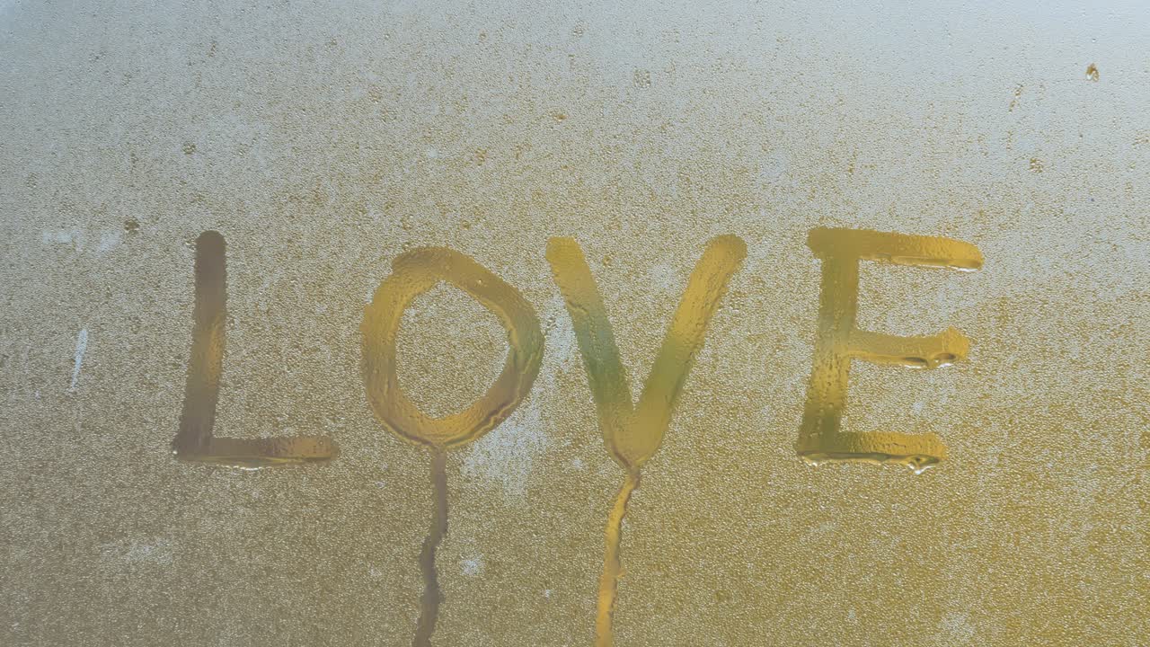 Water droplet falls down the glass with LOVE written on dewy surface - 4K.