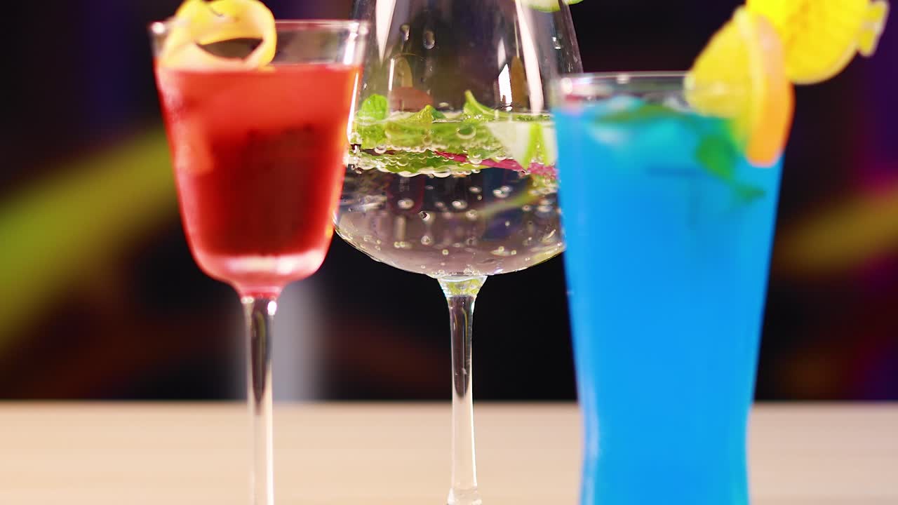 Vibrant cocktails displayed on a bar counter with dynamic camera movement, highlighting colorful drinks and garnishes in a lively setting