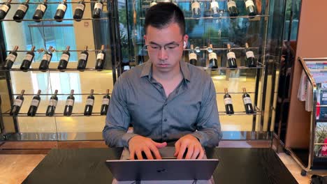 hombre millennial asiático concentrándose en el trabajo de computadora portátil en una casa de lujo con exhibición de vino