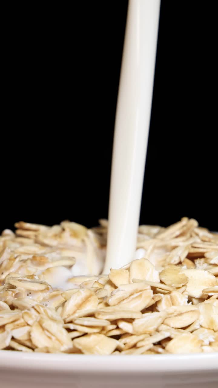 Latte che scende a cascata sui cereali d'avena in una ciotola, creando una dinamica scena per la colazione con uno sfondo nero.