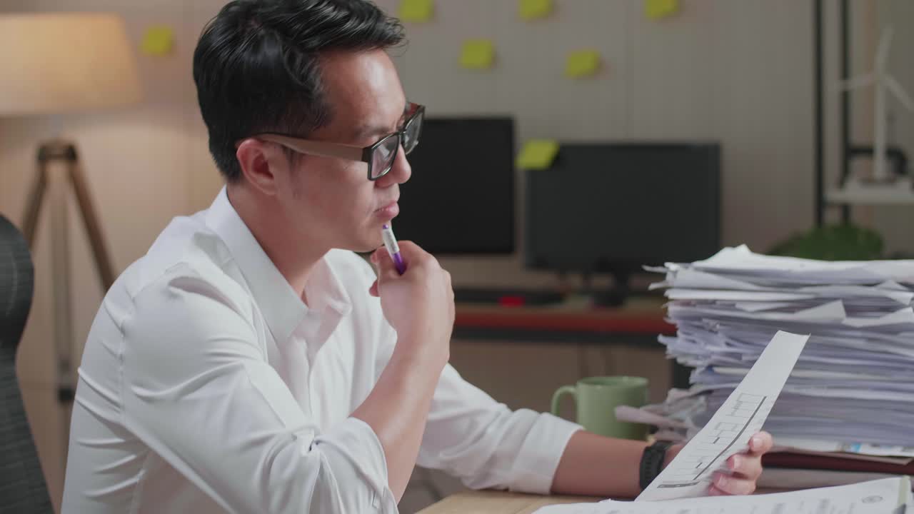 Close Up Of Asian Man Thinking And Looking At Paper Then Raising Index Finger While Working With Documents At The Office