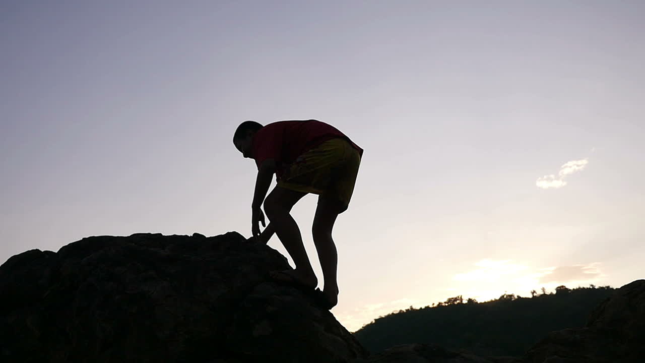 Boy Climbing a Rock at Sunset
