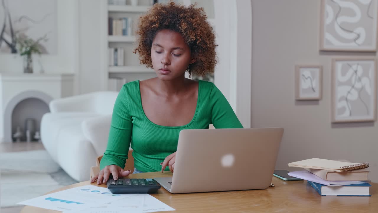 Jovem mulher de negócios afro-americana usando calculadora sentada no escritório em casa