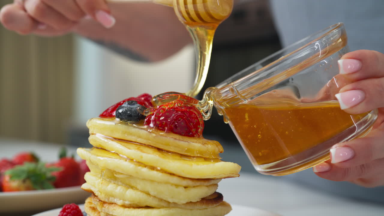 Woman pouring honey on delicious pancakes with fruit in slow motion