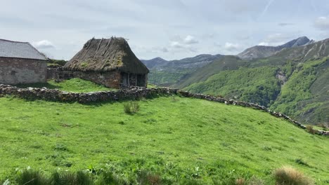 Panorámica-A-La-Derecha-Que-Revela-Una-Cabaña-Tradicional-Con-Techo-De-Paja-En-Medio-De-Un-Espectacular-Valle-Verde-En-Asturias,-España