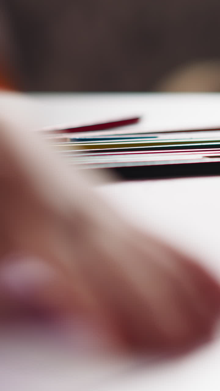 Hand of little painter draws illustration on paper sheet at art lesson in classroom focus on set of multicolored pencils closeup slow motion