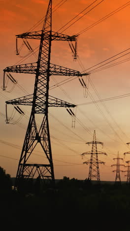 electric towers against orange sky at sunset. high-voltage electricity pylons in the evening. panoramic view of transmission lines. camera rising. vertical video